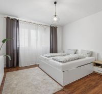 A bright bedroom with a double bed, wardrobe, wood-patterned flooring, and subtle lighting in a 3-room apartment.
