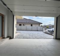 An open garage in a family house with a view of a paved yard.