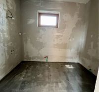 Unfinished room in a family house with a concrete floor and a small window.