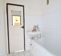 A bathroom in a 3-room apartment with simple white tiles and a bathtub.