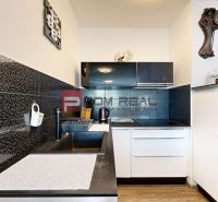 A kitchen in a 2-room apartment with dark tiles and a wooden decor floor.