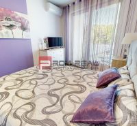 A double bed with purple accessories and a TV in a 2-room apartment with a wood-patterned floor.