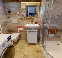 A bathroom in a 2-room apartment with a washing machine, shower, and ceramic tiles.