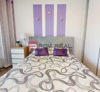 A bedroom with purple accessories, light furniture, and a wooden decor floor in a two-room apartment.