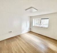 A room with a wood-patterned floor in an office, empty, with a window and white walls.