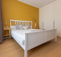 Bedroom in a 2-room apartment with wood-patterned flooring, yellow wall, white bed.