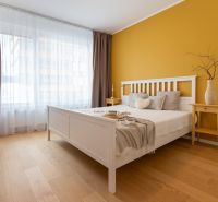 A bedroom in a two-room apartment with a wooden floor decor and a yellow wall.