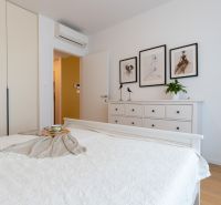 A bedroom in a two-room apartment with white furniture and a wooden decor floor.