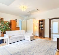 A living room in a family house with a white sofa, wooden cabinets, and a floor with a wooden decor.