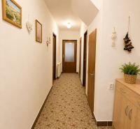 A hallway in a family house with a patterned carpet, wall decorations, and wooden furniture.