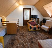 Attic room in a family house with armchairs, a television, and a carpet.