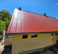 A family house with a red roof in Banky, surrounded by nature and a blue sky.