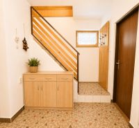Interior of a family house with a wooden staircase and a chest of drawers on the tiles.