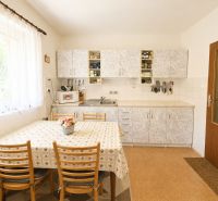 A kitchen in a family house with white cabinets, a dining table, and a window with a white curtain.