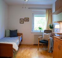 A room in a 3-room apartment with a bed, a wooden-decor floor, and a table with a lamp.