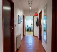 A hallway in a 3-room apartment with tiles leads to a room with flowers on the table.