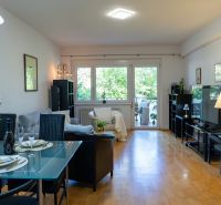 Living room of a three-room apartment with a wood-decor floor and a dining area.
