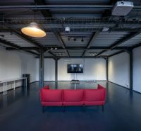 An office with a red couch, a television, and metal ceilings.
