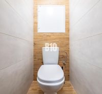 A toilet with ceramic tiles and a wooden decor floor in a studio apartment.