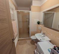 Bathroom in a 2-room apartment with a sink, shower, and washing machine, tiles in a beige shade.
