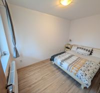 A bedroom with a wood-patterned floor in a two-room apartment, bed by a white wall.