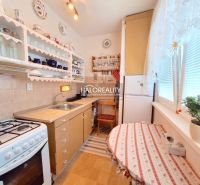 A kitchen in a 2-room apartment with wooden decor, flowers, and a dining table.