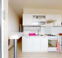 A kitchen in a 2-room apartment with white cabinets, a gas stove, and a floor with a wood design.