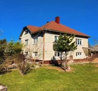 A family house in Nové Hony with a red roof, surrounded by a garden with coniferous trees.