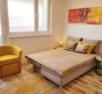 A one-room apartment with a bed, a yellow armchair, and a floor with a wooden decor.