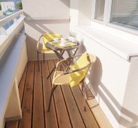 A balcony with a wooden decor floor, chairs, and a table in a studio apartment.