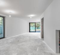 A spacious room with light walls, concrete flooring, and large windows in a family house.