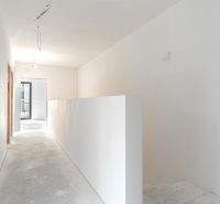 A hallway in a family house with white walls and a bare concrete floor surface.