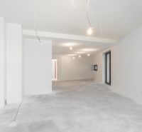 A spacious unfurnished interior of a family house with white walls and a raw floor.