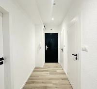 A hallway with light walls, white doors, and a wooden decor floor in a 3-room apartment.