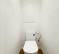 A toilet with a wood-patterned floor in a three-room apartment, white walls, and a concealed tank.