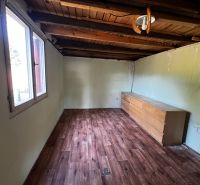 A room in a cottage with a wooden decor floor, a dresser, and a window on the wall.