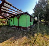 A garden cottage with a green facade and a terrace in the garden of Lozorno surrounded by trees.