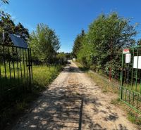 A country road leading through gardens in Lozorno, surrounded by green trees and fences.