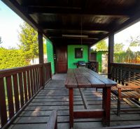 A wooden terrace with a bench and table in the gardens in Lozorno, surrounded by green shrubs.