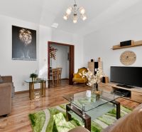 Living room in a two-room apartment with a sofa, an armchair, a television, and a floor with a wooden decor.