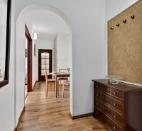 A hallway in a 2-room apartment with a wooden decor floor, a mirror, and a table in the background.