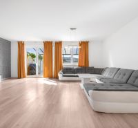 Living room in a family house with a sofa, orange curtains, and a wooden decor floor.