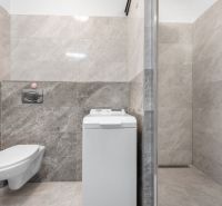 A bathroom in a family house with a washing machine and a shower, tiled with marble tiles.