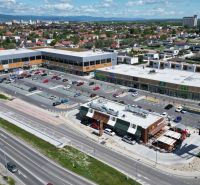 A shopping center with a parking lot in Bratislava - Podunajské Biskupice surrounded by residential buildings.