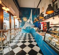 A café with a black and white floor, the Eiffel Tower on the wall, bright lights, wooden chairs.