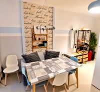 Dining area in a studio apartment with colorful chairs and a decorative wall.