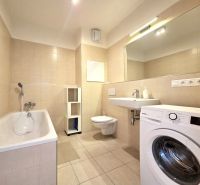 A bathroom with a bathtub, washing machine, sink, and toilet in a 2-room apartment.