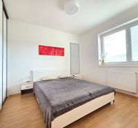 A bedroom in a two-room apartment with a wooden decor floor and minimalist furniture.