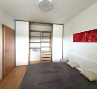 A bedroom in a 2-room apartment with a wooden decor floor, a built-in wardrobe, and an abstract painting.