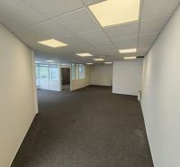 Offices with white walls and carpet, illuminated by ceiling lights.